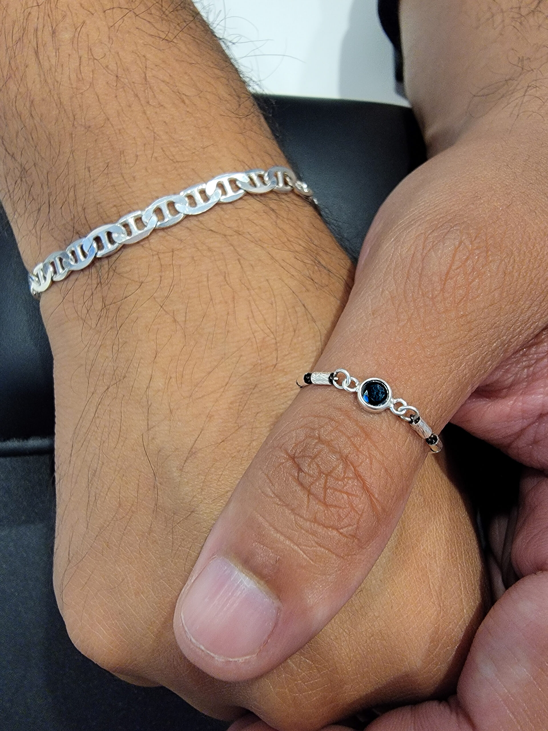 Permanent jewelry thumb ring and silver chain bracelet on the same man, featuring a minimalist black stone detail.